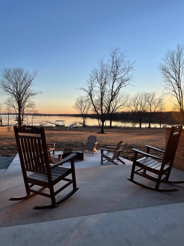 Un área de patio con sillas Adirondack y una chimenea, con vista a un lago.
