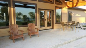 Un patio con dos sillas de madera tipo Adirondack, una mesa con sillas de mimbre y una hamaca.