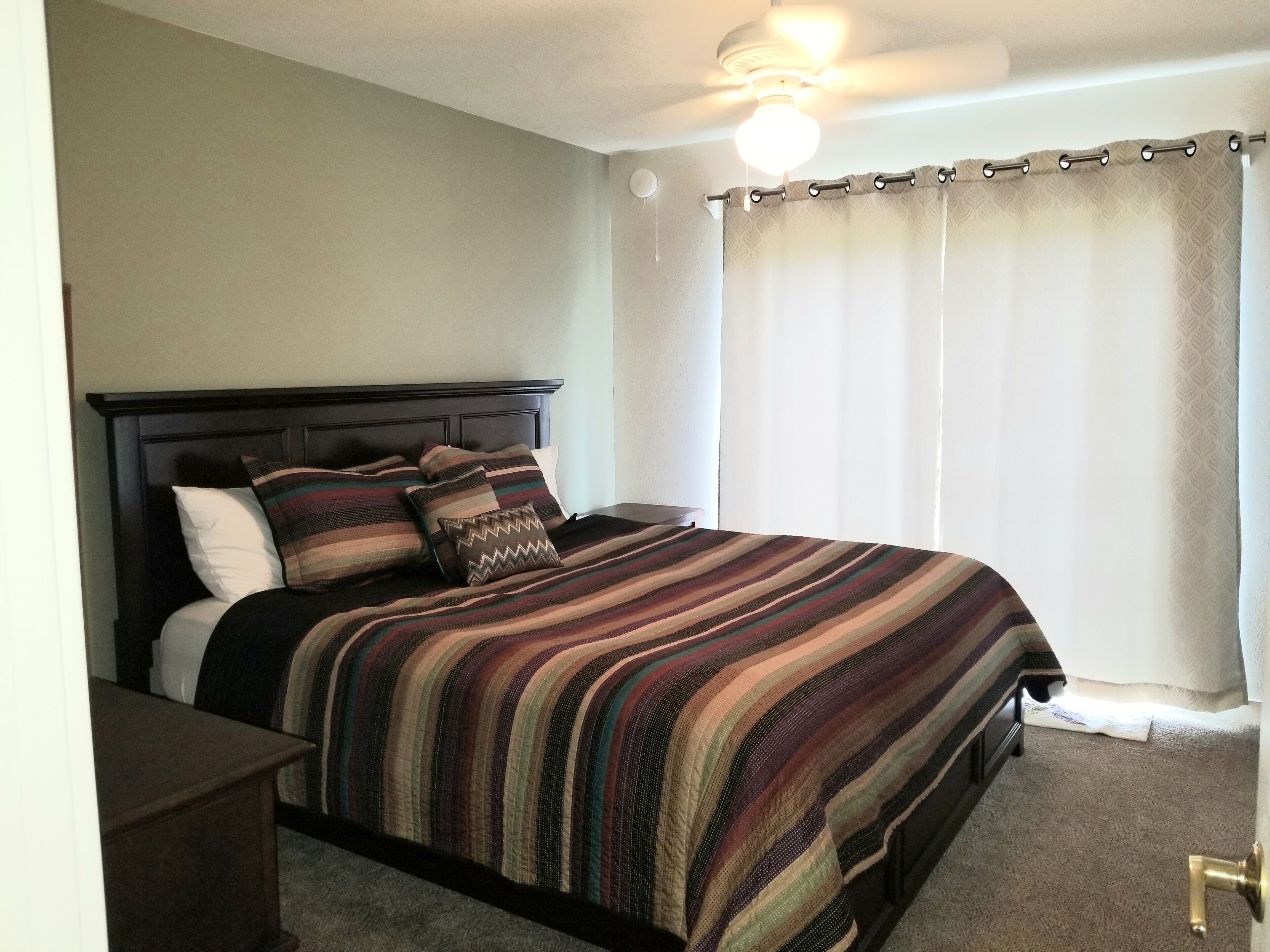A neatly made bed with a striped bedspread, a dark headboard, and a bedside table.