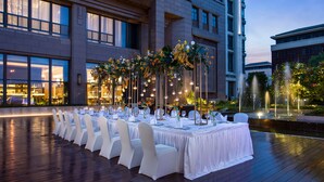 Een buitenmeedeel met tafels gedekt voor een formeel evenement, omringd door moderne gebouwen.