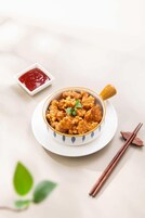 Un plato de comida frita con un recipiente pequeño de salsa a un lado, sobre un plato blanco con diseño de hojas.