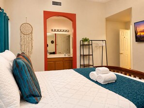 Une chambre d’hôtel avec un lit, une coiffeuse avec un miroir, un attrape-rêves et un tableau au mur.