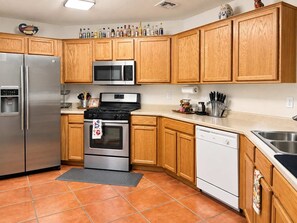 Una cocina con armarios de madera, electrodomésticos de acero inoxidable, microondas, estufa y lavavajillas.