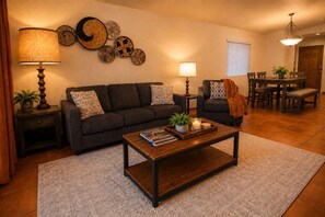 Una sala de estar con sofá, mesa de centro, lámparas y decoración en la pared.