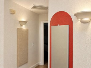 Un pasillo con pared beige texturizada, una lámpara y una puerta con detalles en rojo.