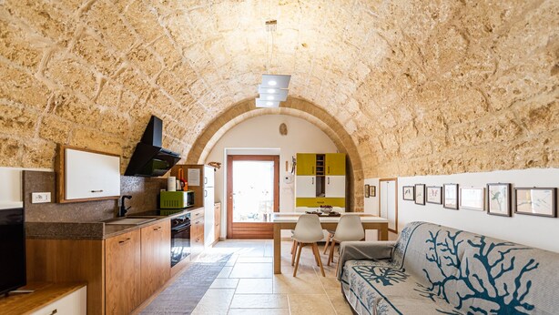 Una cocina acogedora con pared de piedra, armarios de madera y zona de comedor con sofá y sillas.