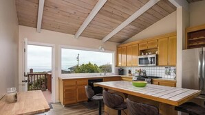 A kitchen with wooden cabinets, a stainless steel refrigerator, and a large island with a green bowl. - Oceanview (Aptos)