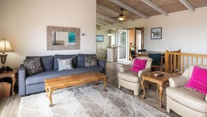 A spacious living room with a high ceiling, a sofa set, a coffee table, and a dining area visible through an open door. - Oceanview (Aptos)
