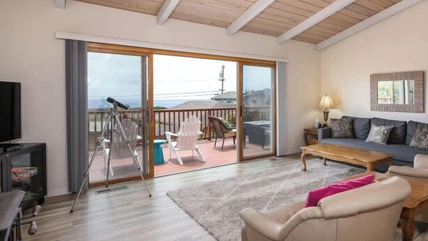 A living room with a large sliding glass door leading to a balcony, a sofa, a coffee table, and a television. - Oceanview (Aptos)