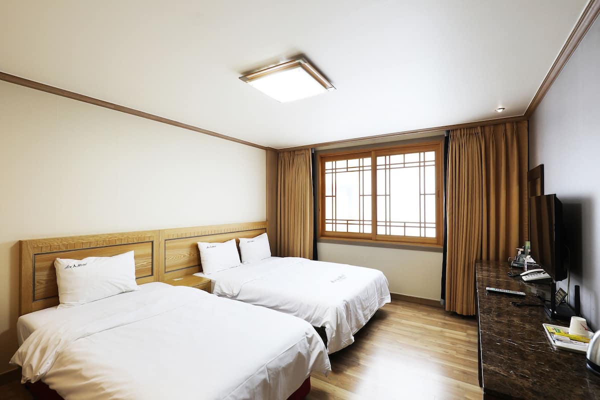 A hotel room with two beds, a desk, a TV, and a window with curtains.