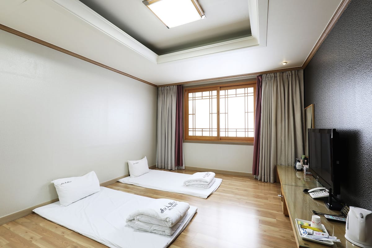 A hotel room with two single beds, a desk with a computer, a TV, and a window with curtains.