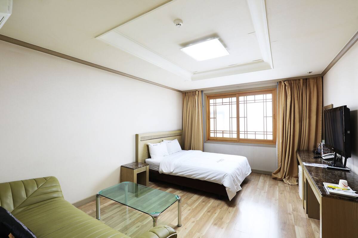 A hotel room with a bed, a desk, a green sofa, a glass table, and a TV.