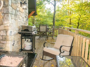 An outdoor patio with a stone wall, a grill, a cushioned chair, and a table. - Misty Mountain Cabin with Grandfather Views (Blowing Rock)