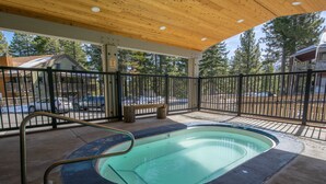 Una piscina scoperta coperta da un tetto in legno, con ringhiera in metallo, e vista su un’area parcheggio e alberi sullo sfondo.