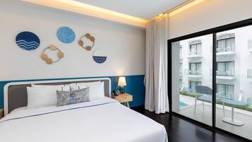 Quarto de hotel com uma cama grande, uma mesinha de cabeceira com abajur e vista para uma piscina e edifícios através de uma janela ampla.