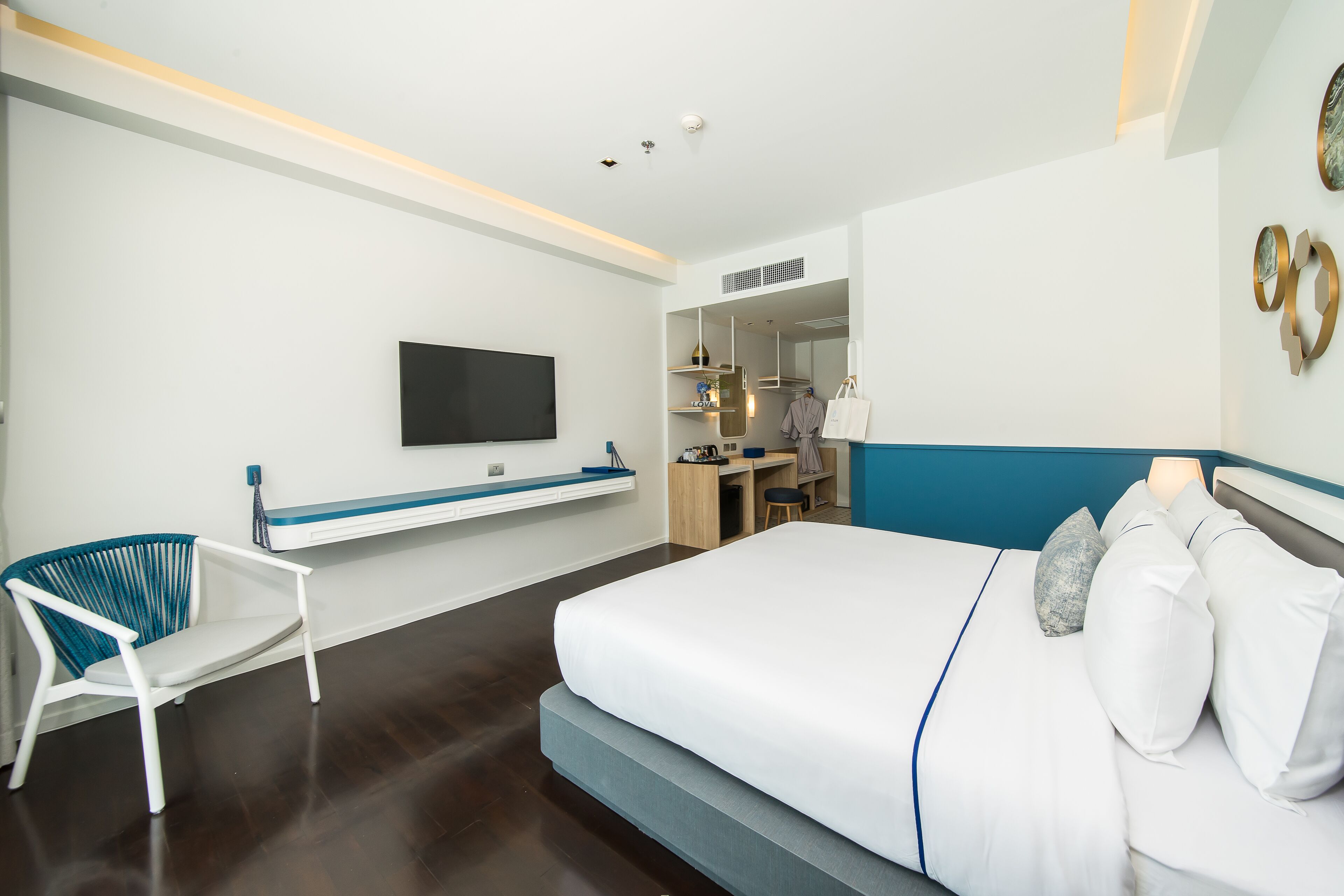 A modern hotel room with a large bed, a desk, a chair, and a flat-screen TV mounted on the wall.