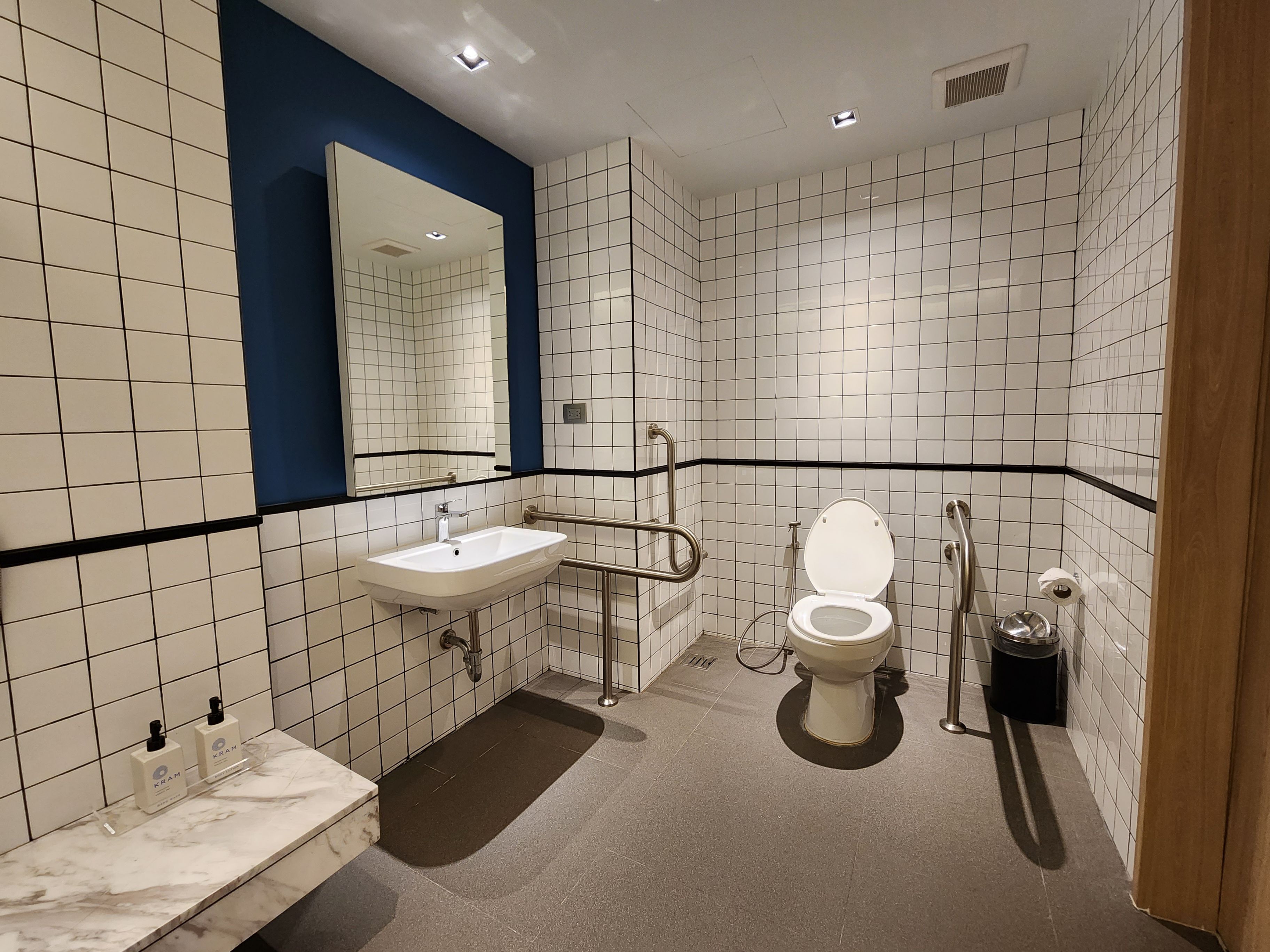 A modern bathroom with white tiled walls, a marble countertop, a white sink, a toilet, and a handheld showerhead.