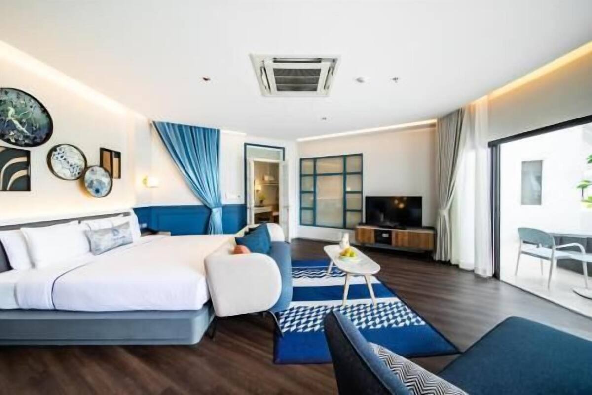 A modern hotel room with a bed, sofa, TV, and a view of the outdoors.