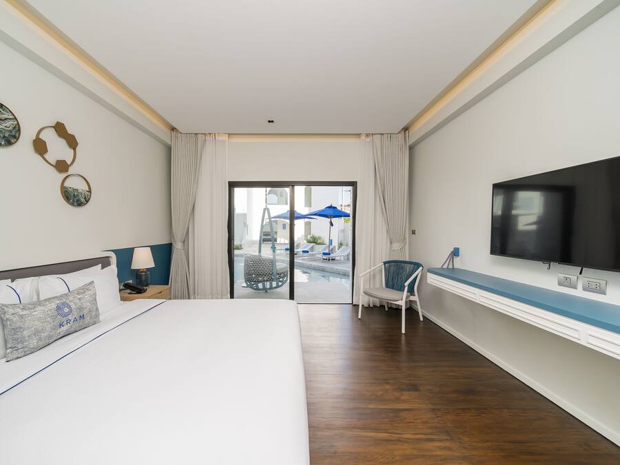 A hotel room with a large bed, a TV, a desk, and a view of the pool area.