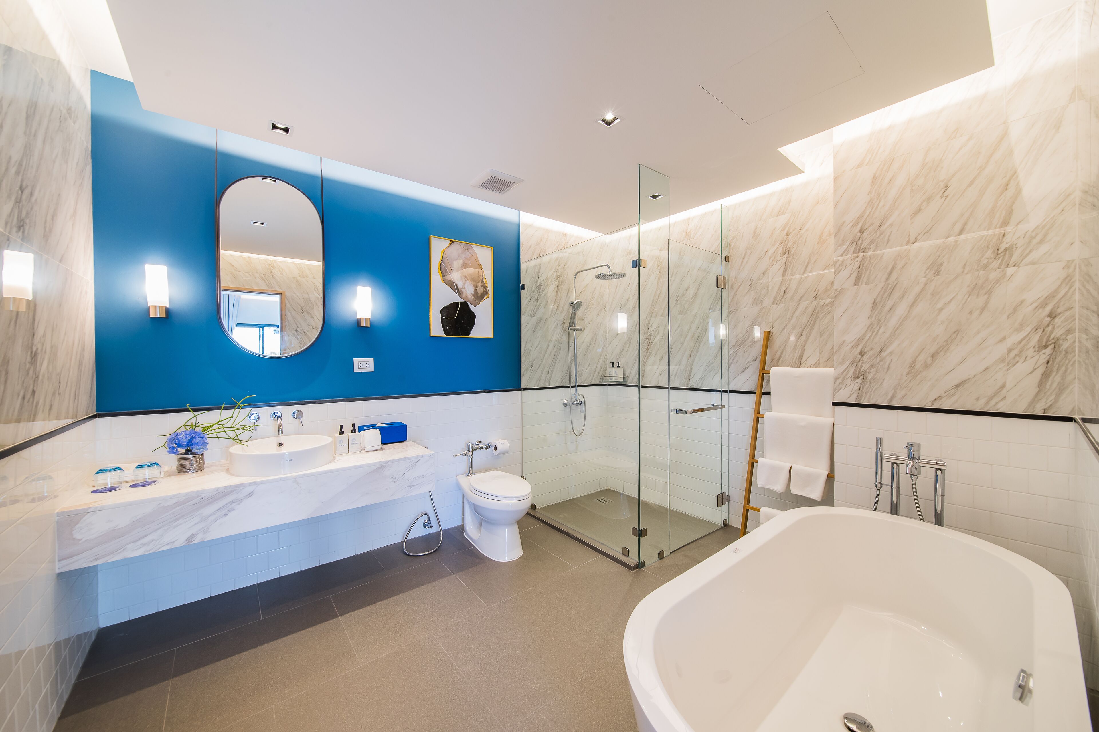A modern bathroom with a large bathtub, a glass-enclosed shower, and a marble-tiled wall.