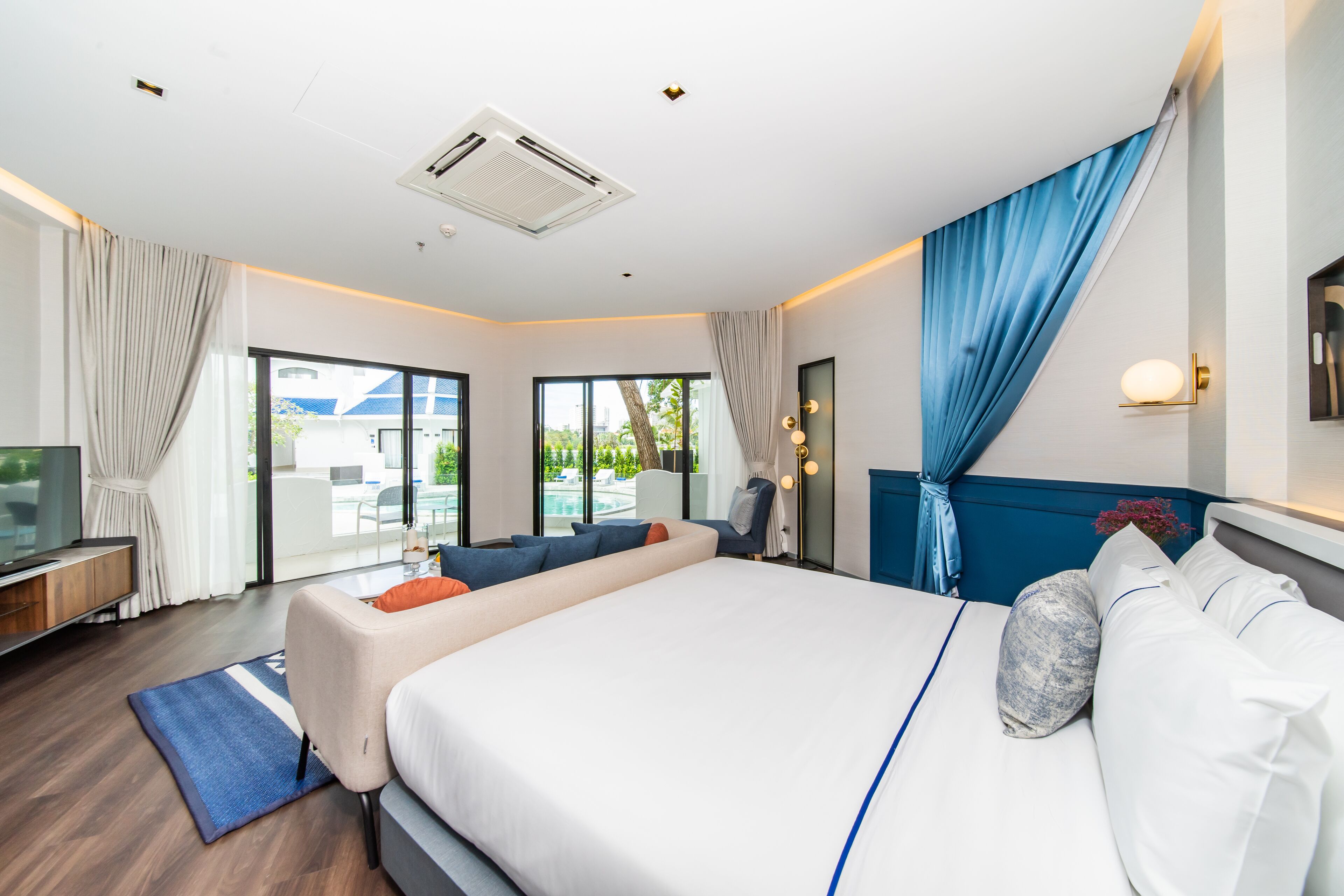 Ein modernes Hotelzimmer mit einem großen Bett, einer Couch, einem Schreibtisch und Blick ins Freie.