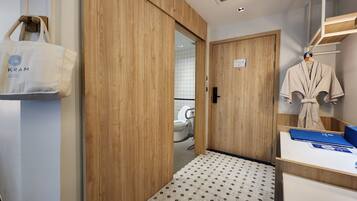 A hotel room with a wooden wardrobe, a robe hanging on the wall, and a tiled floor.