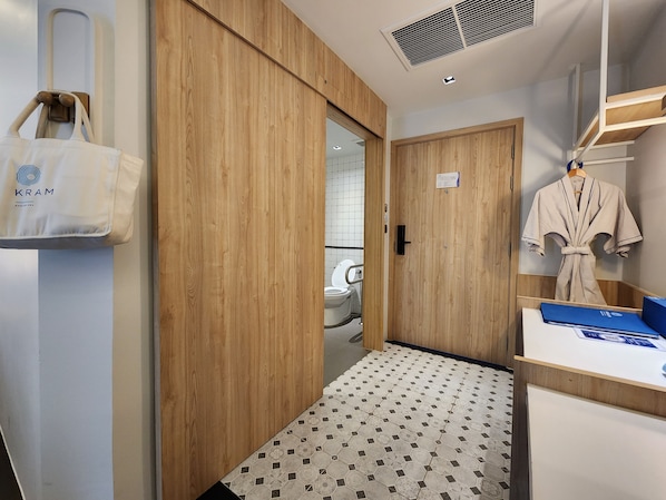 A hotel room with a wooden wardrobe, a robe hanging on the wall, and a tiled floor. - Kram Pattaya (Pattaya)