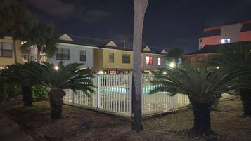 A residential area at night with houses, a swimming pool, and palm trees.