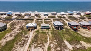 Una zona costera con varias casas frente a la playa, algunas con estructuras elevadas, y una carretera que atraviesa la propiedad.