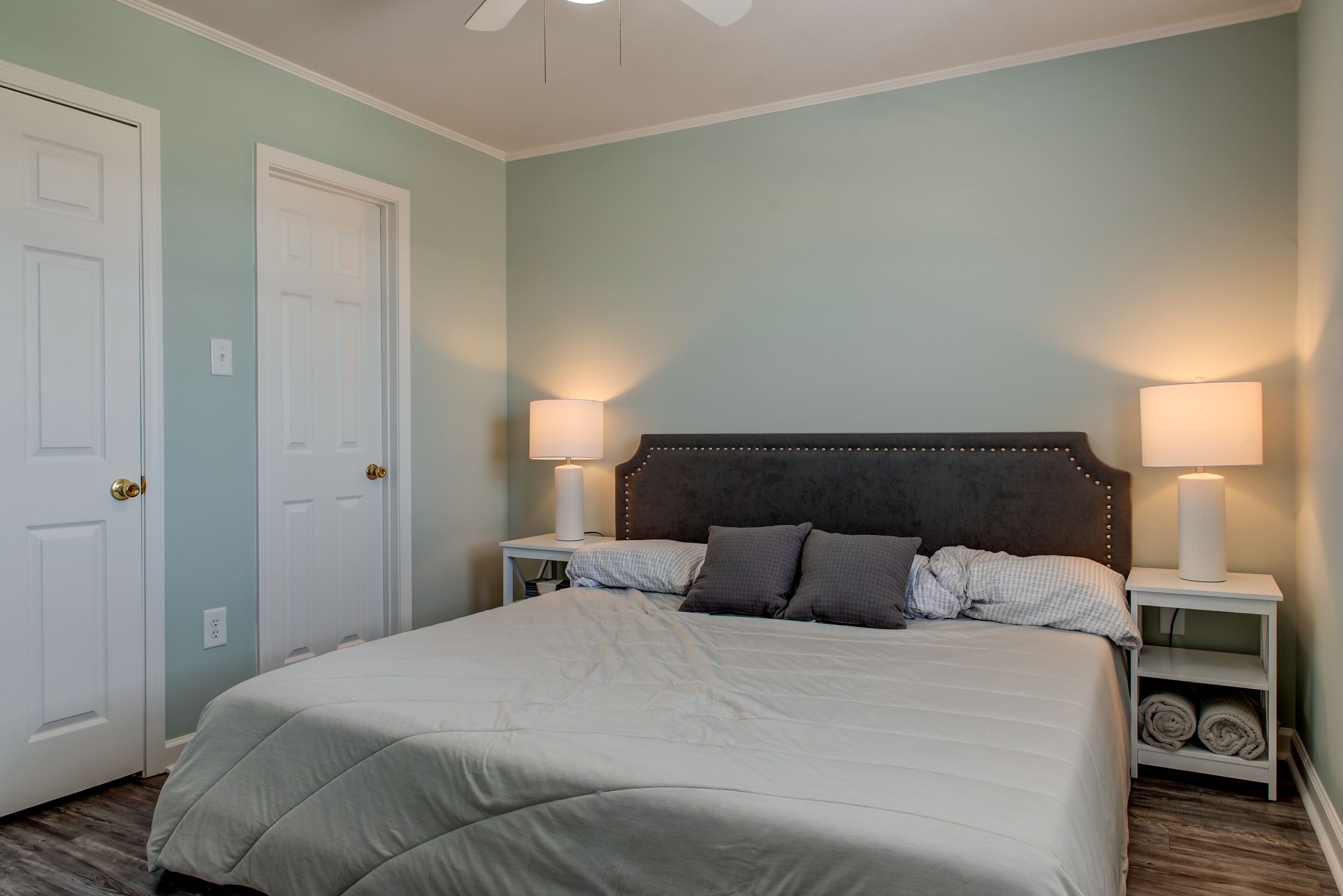 A bedroom with a bed, two bedside lamps, a headboard, and a white door.