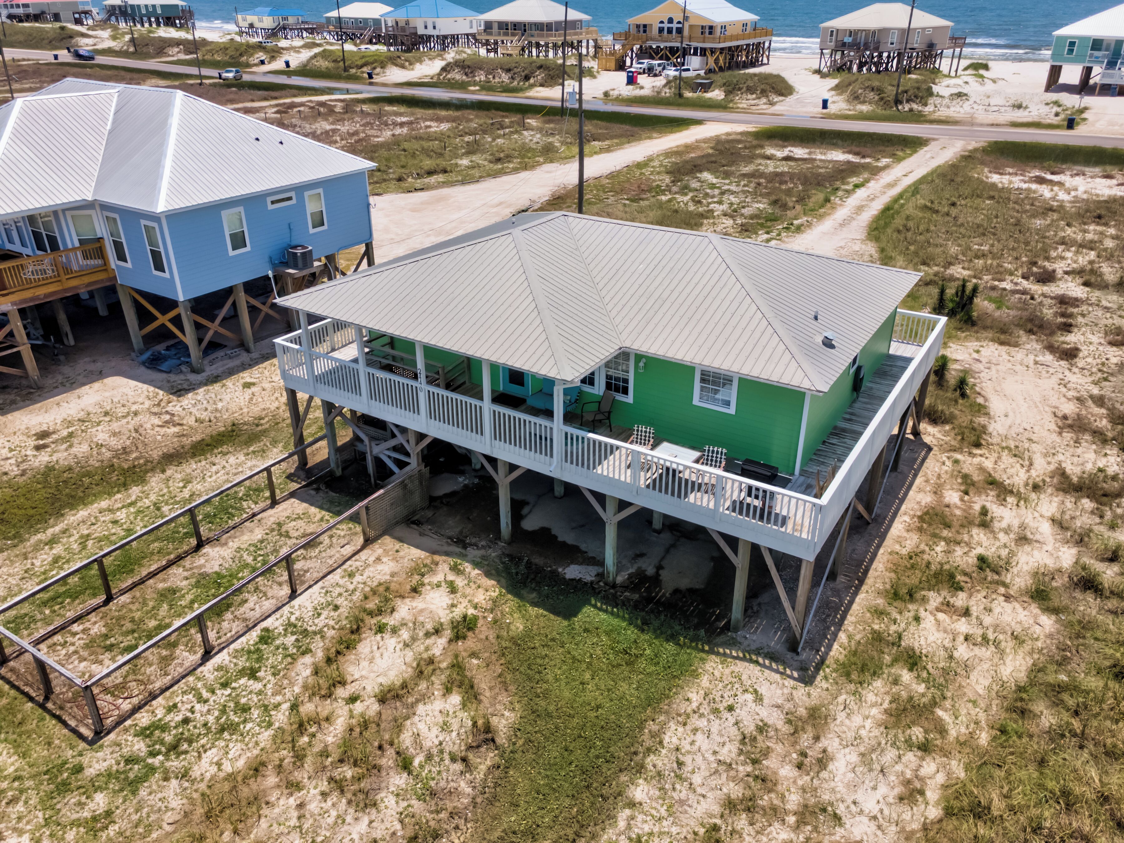 A beachfront house with a balcony, elevated on stilts, and a view of the ocean.