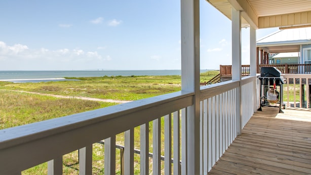 Una terraza de madera con vista al océano y la playa.