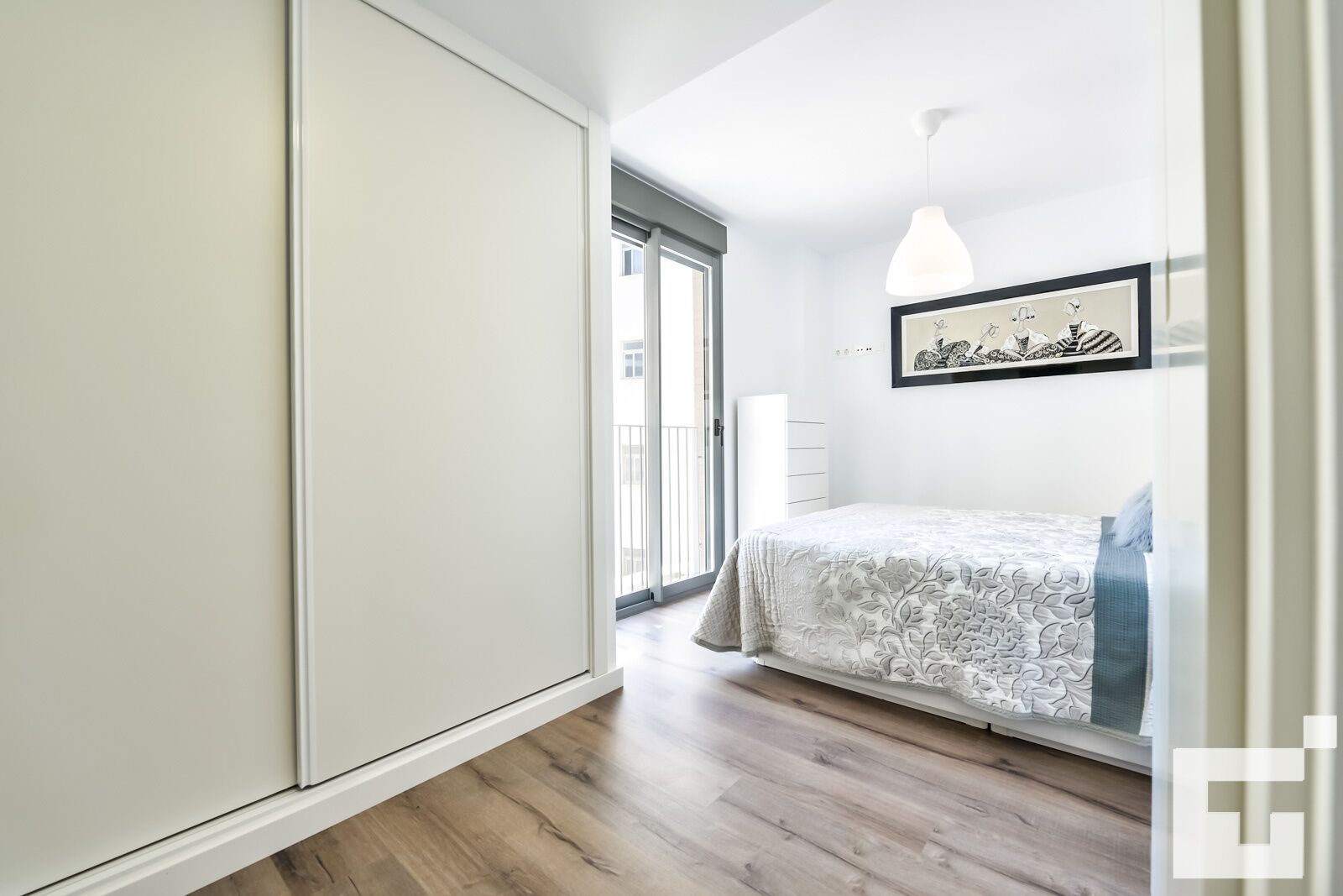 A bedroom with a bed, a wardrobe, a door leading to a balcony, and a framed picture on the wall.