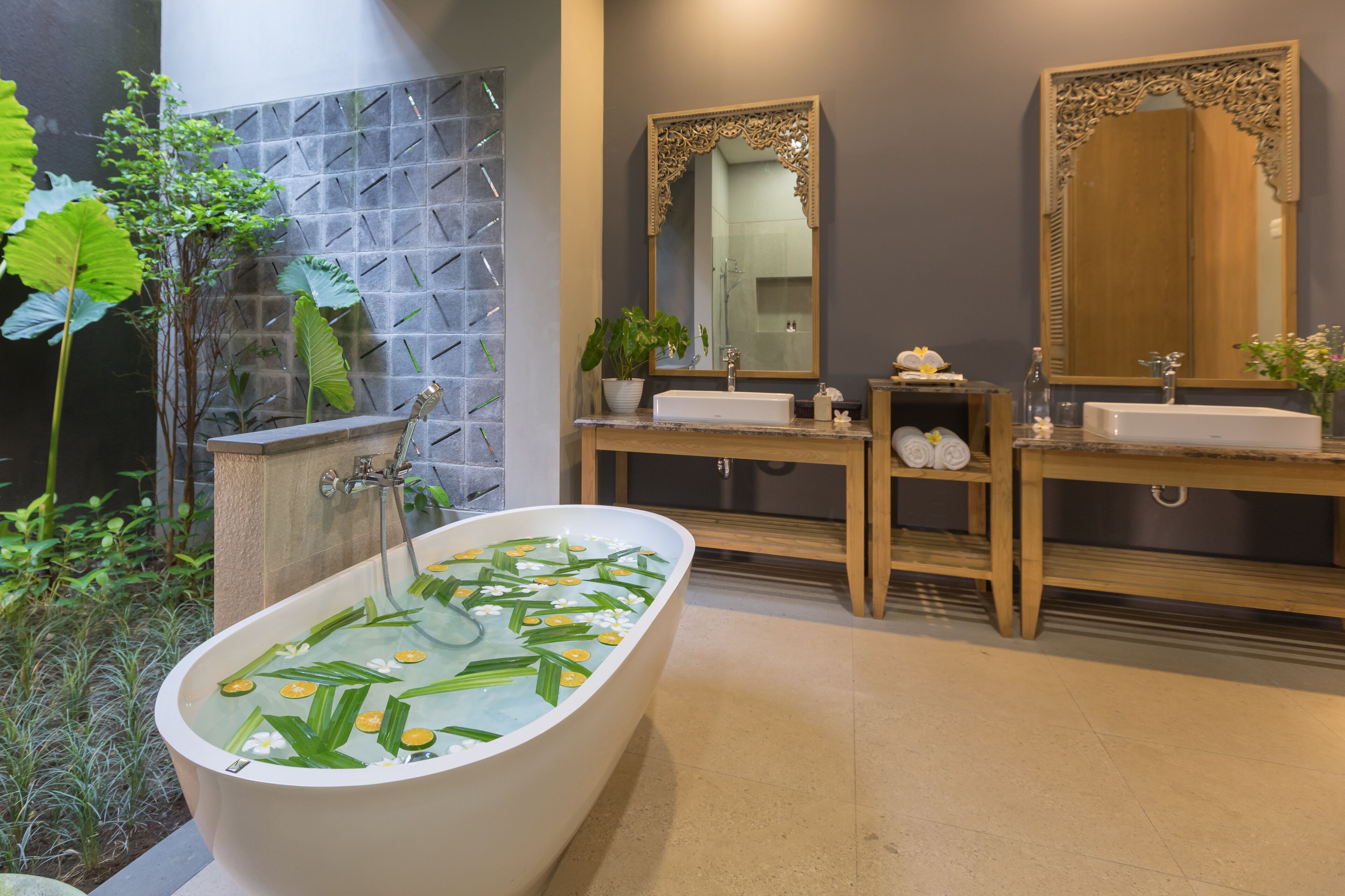 A modern bathroom with a freestanding bathtub, two sinks, a large mirror, and a decorative wall.