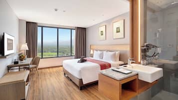 Ein Hotelzimmer mit einem großen Bett, einem Schreibtisch mit Stuhl, einem Badezimmer mit Dusche und Blick auf die Landschaft.