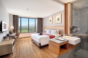 Une chambre d’hôtel avec un grand lit, un bureau avec une chaise, une salle de bain avec douche et une vue sur le paysage.