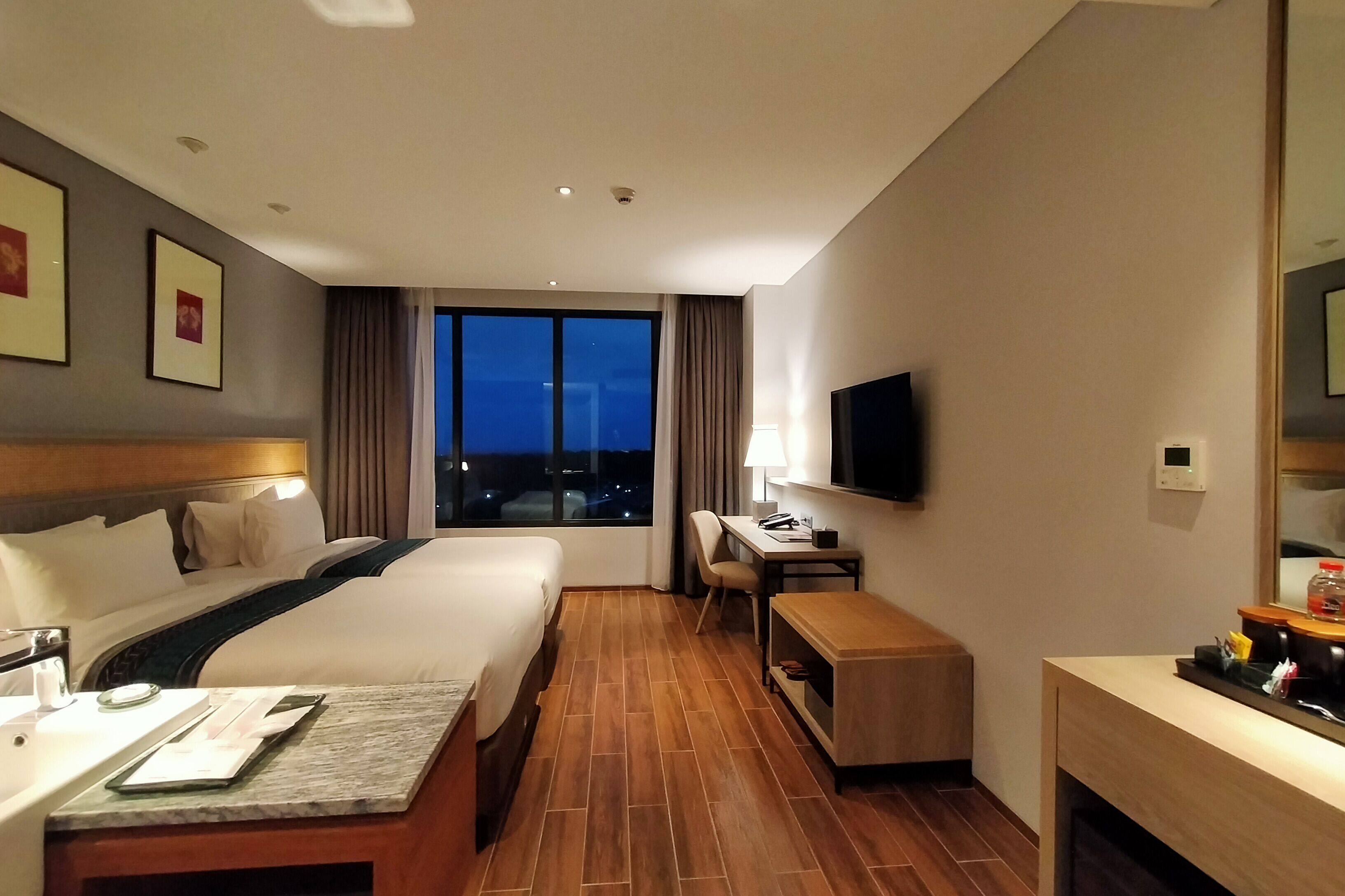 Een hotelkamer met een groot bed, een bureau, een stoel, een televisie en een raam met uitzicht 's nachts.