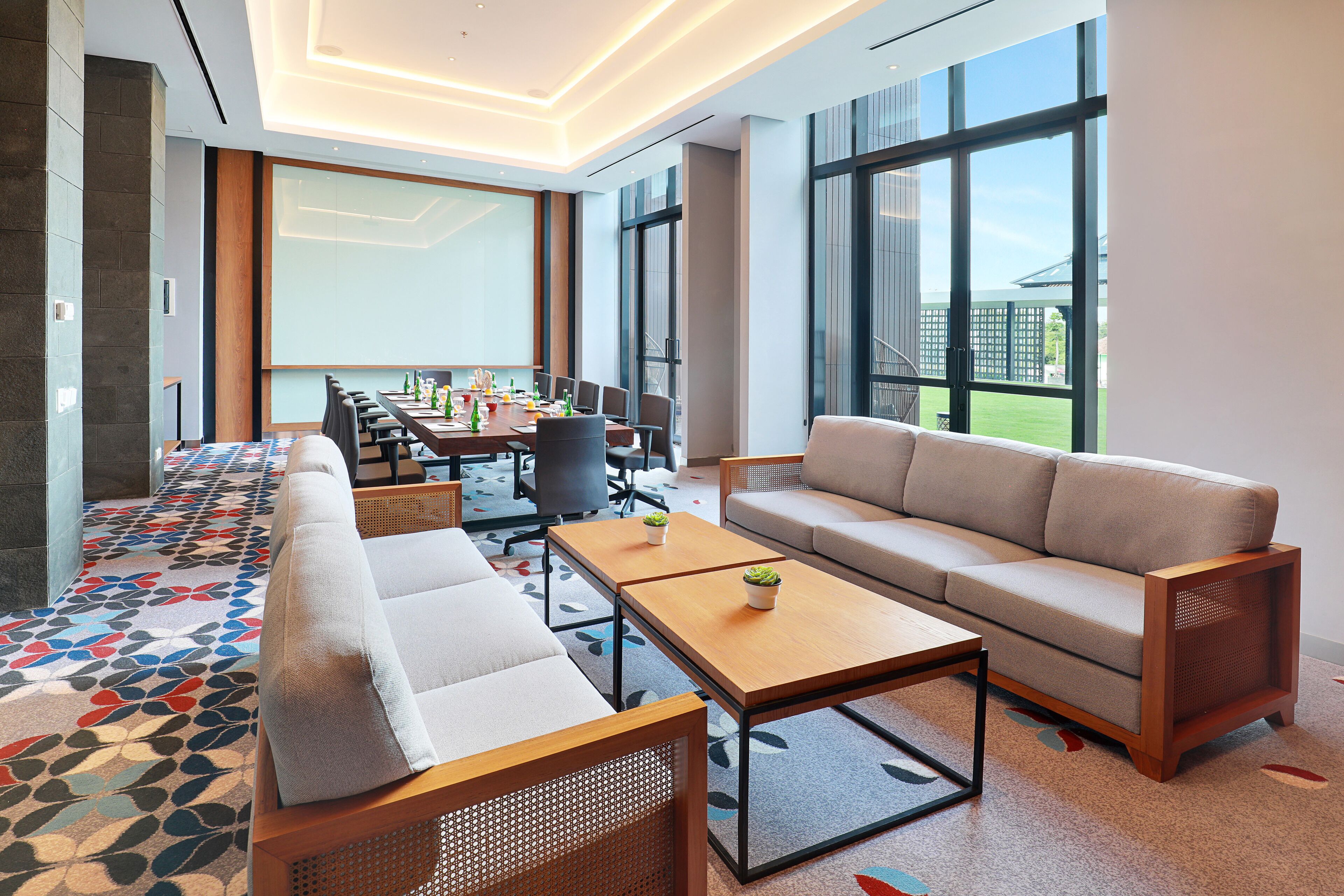 A modern hotel room with a sofa, a coffee table, and a dining area with a table and chairs.