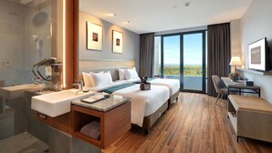 A hotel room with a large bed, a desk, a chair, a bathroom with a sink, and a large window offering a view.