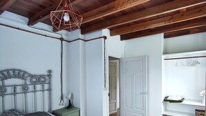 Une chambre avec un plafond en bois, un lit avec une literie blanche, une table de chevet et un luminaire suspendu.