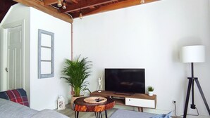 Un salon moderne avec un plafond en bois, un canapé gris, un téléviseur, une petite table et un lampadaire.
