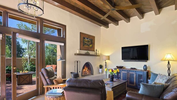 A cozy living room with leather furniture, a fireplace, a television, and a large window overlooking a garden. - Stylish and Serene, Community Pool (Santa Fe)