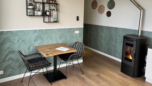 Ein gemütliches Zimmer mit einem Holztisch und zwei Stühlen, einem an der Wand befestigten Regal mit Dekoration und einer wandmontierten Uhr, sowie einem modernen Kamin.