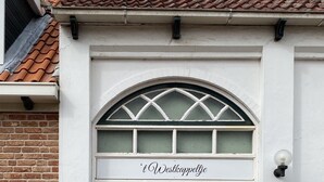 Ein Gebäude mit einer dunkelgrauen Tür, einem Schild über der Tür mit der Aufschrift „Westkappetje“ und einem Ziegeldach.