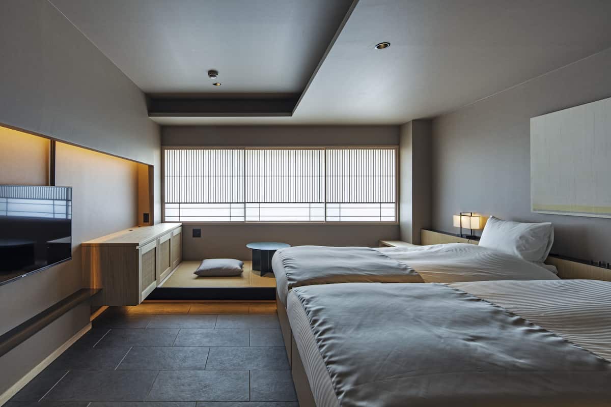 Una habitación de hotel moderna con cama, mesita de noche y ventana con persianas.