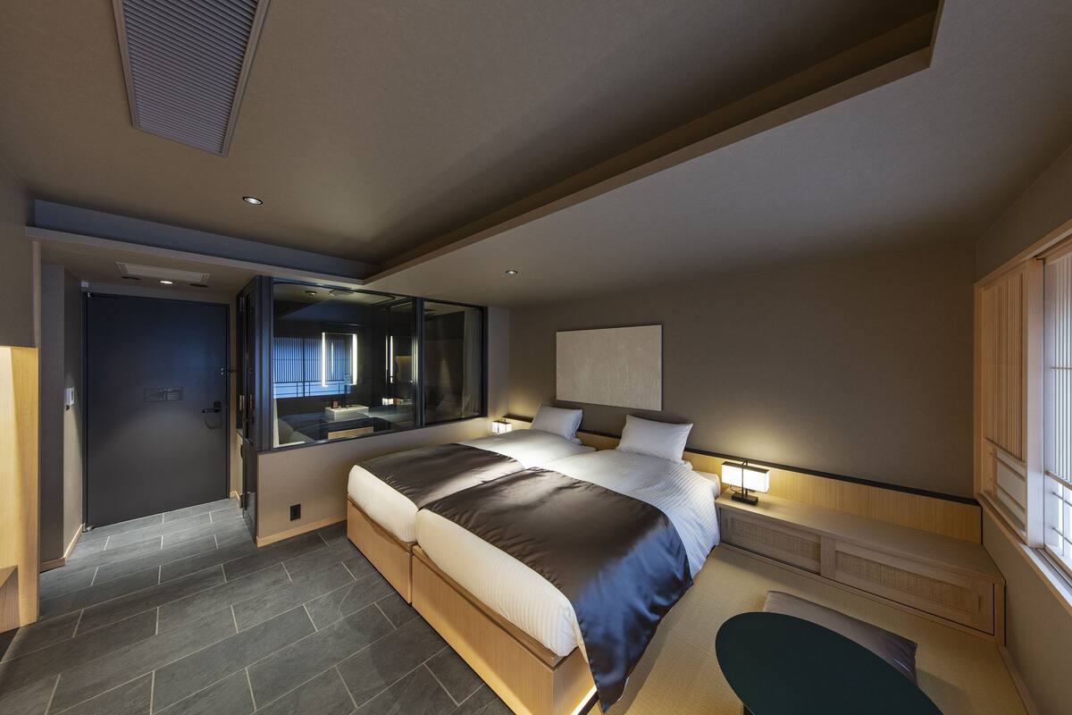 Un dormitorio moderno con una cama grande, una mesita de noche con lámpara, un banco empotrado y un ventanal amplio.