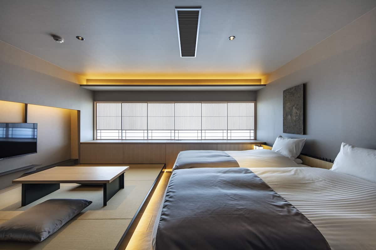 Una habitación de hotel moderna con una cama grande, televisión, ventana con persianas y una mesita de noche.