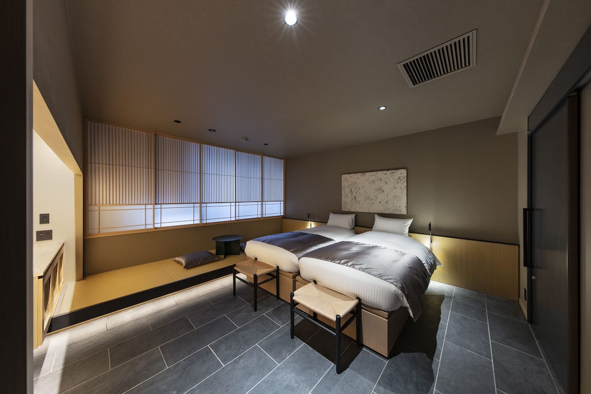 Un dormitorio moderno con una cama grande, una banca empotrada, una mesita pequeña y un panel corredizo estilo shoji.