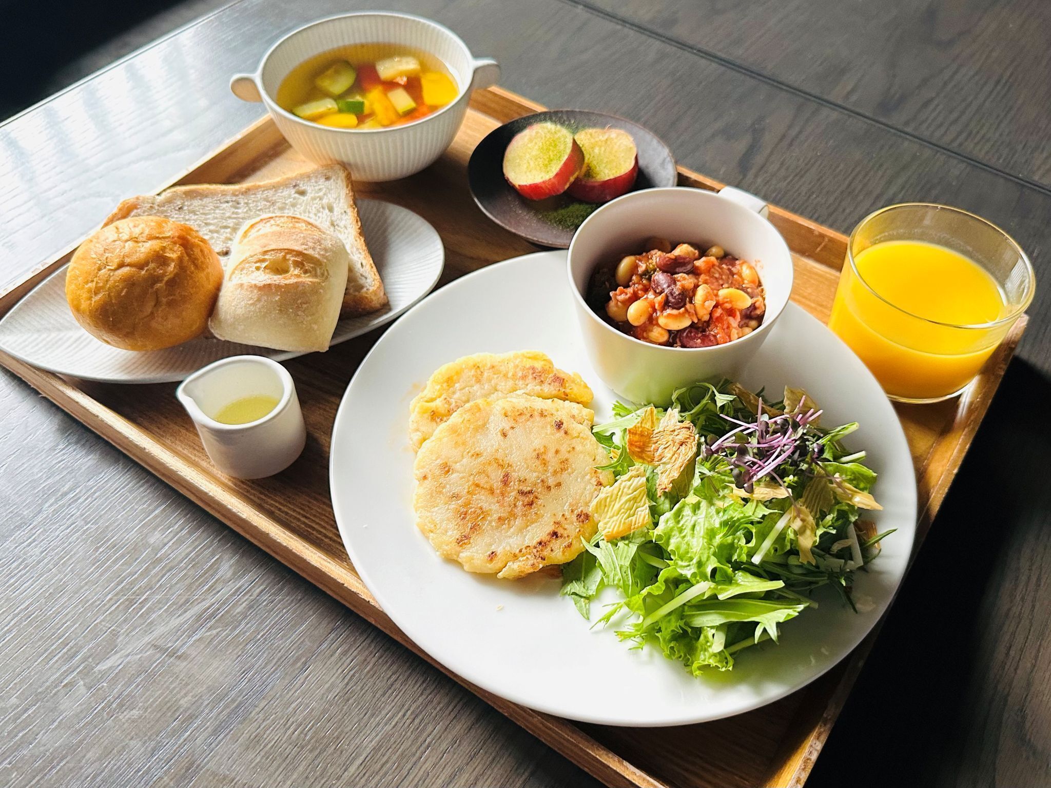 Un vassoio con prodotti per la colazione, tra cui pane tostato, zuppa, fagioli, insalata e succo di frutta.