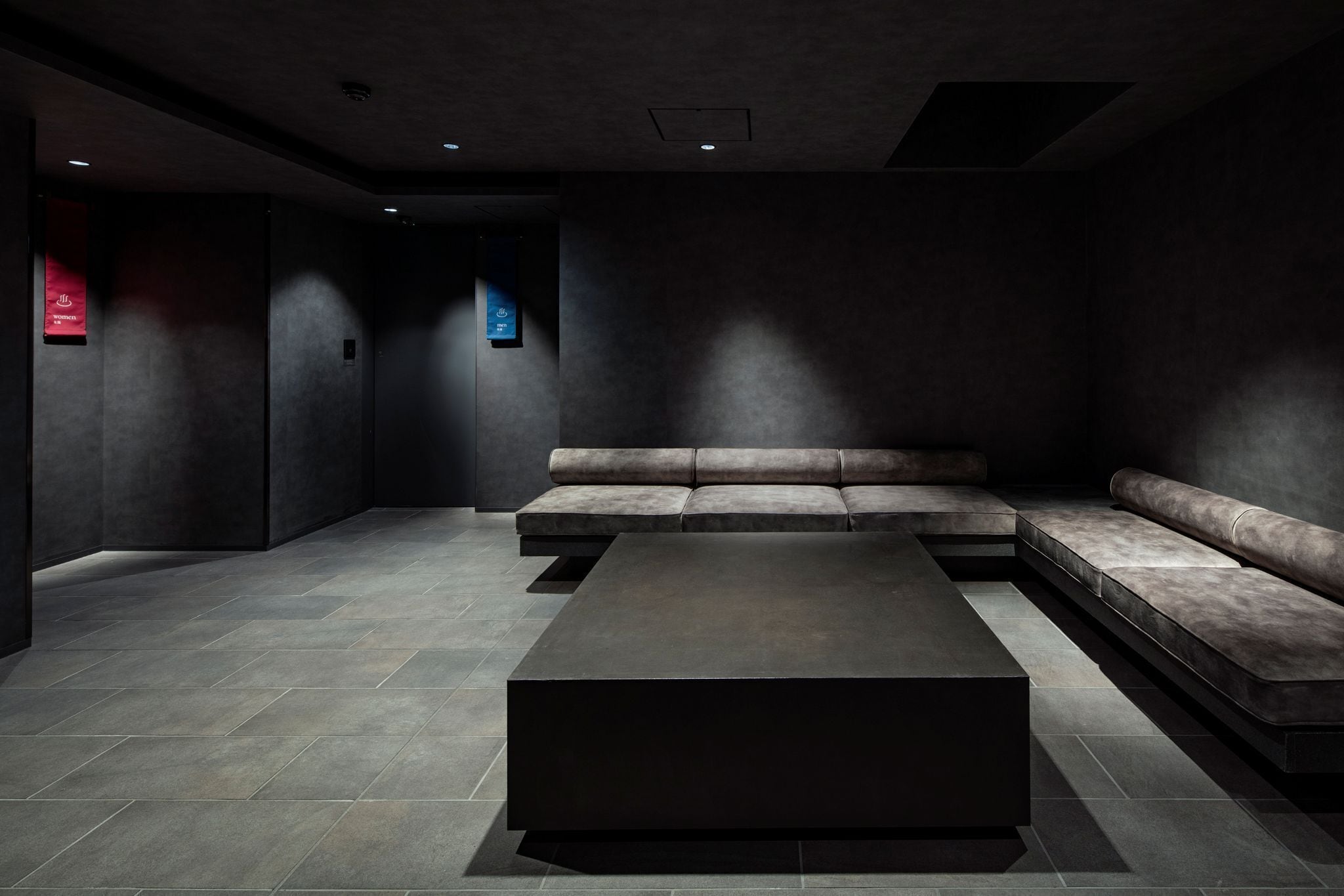 A modern, dimly lit room with a dark-colored sofa and a large, dark coffee table.